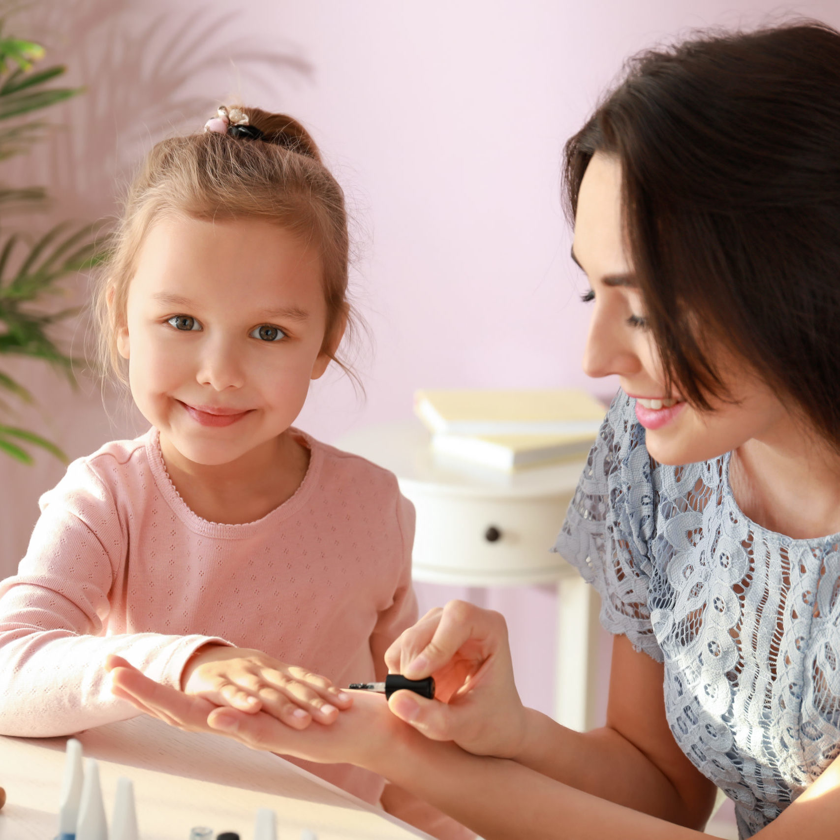 Cute daughter with mother making manicure at home